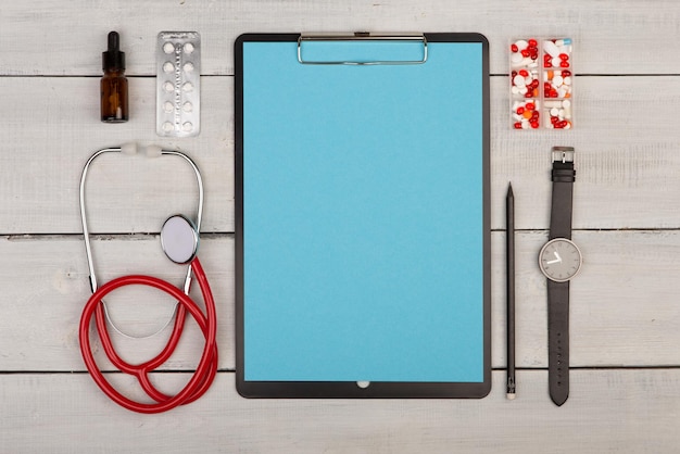 Blank clipboard pills stethoscope and watch on wooden background