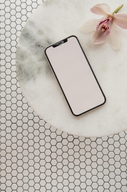 Foto schermo del percorso di ritaglio vuoto telefono cellulare fiore rosa su tavolo in pietra di marmo su sfondo di piastrelle a mosaico modello estetico con spazio mockup vista dall'alto piatta