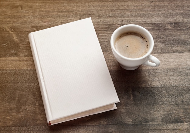 Blank closed booklet, pencil and coffee cup on vintage wood background. Responsive design mockup.