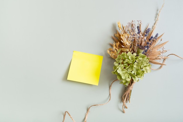 Blank colored paper for notes and a bouquet of dry flowers and herbs on a colored background