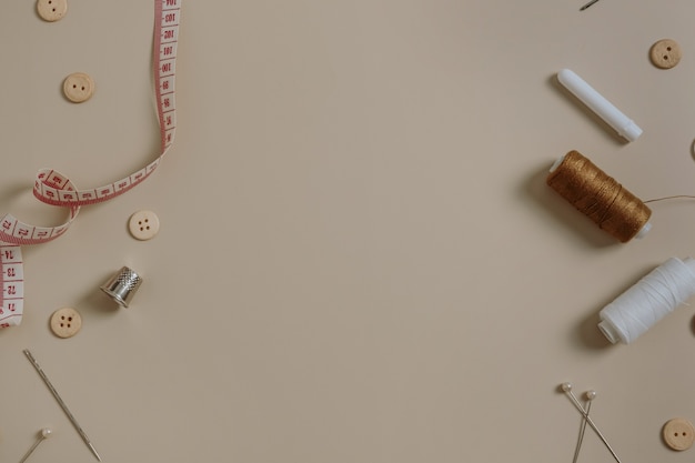 Фото Пустое место для копирования со швейными инструментами: пуговицы, катушка, наперсток, рулетка, иглы на нейтральном бежевом цвете.