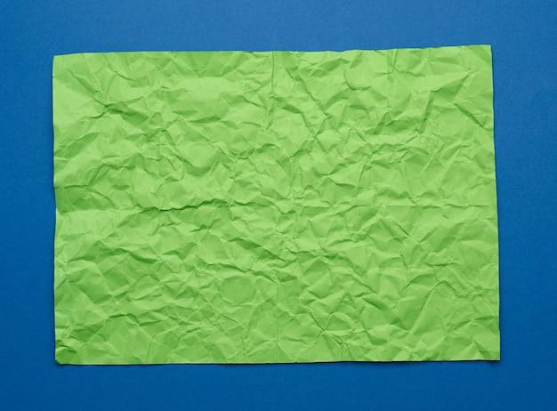 青い背景の上の空白のしわくちゃの緑の紙