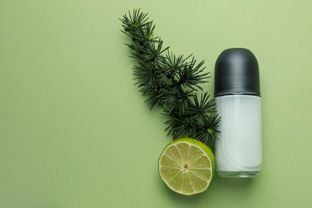 Blank deodorant, spruce twig and lime on green background