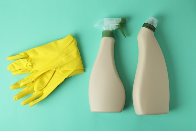 Blank detergent bottles and gloves on mint background