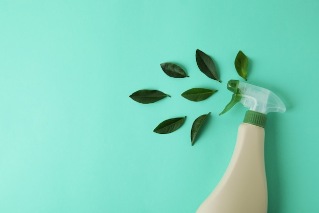 Photo blank detergent spray bottle and leaves on mint isolated background