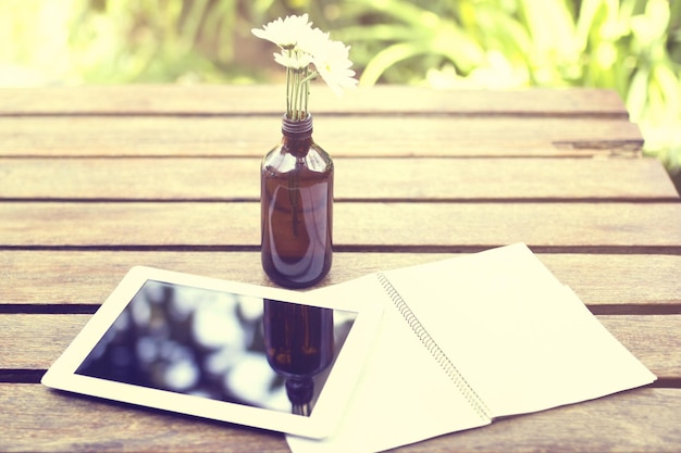 Blank diary with digital tablet and flowers on a wooden table outside