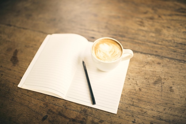 Blank diary with pen and cup of coffee on a wooden table