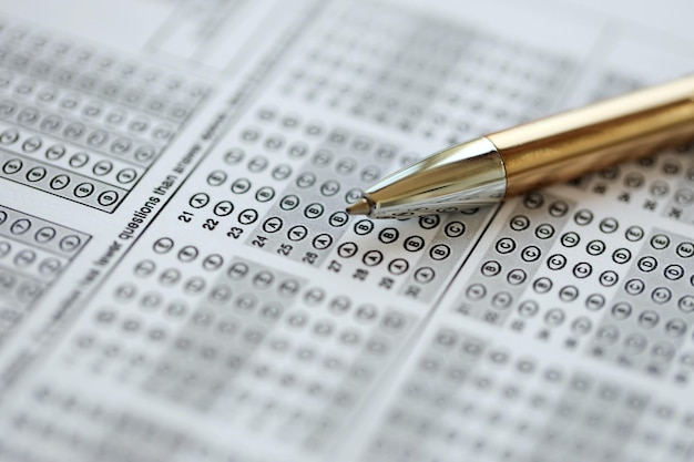 Blank educational test for students lies on table in classroom with pen close up