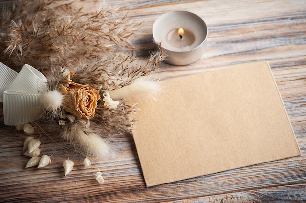 Blank envelope and lit aroma candle and dry flowers on rustic