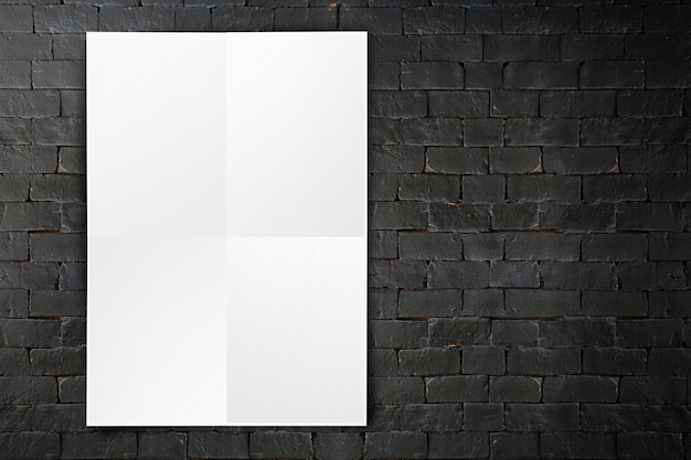 Blank folded paper poster hanging on black brick wall