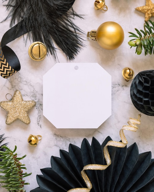 Blank gift tag between black and golden Christmas decorations top view Mockup