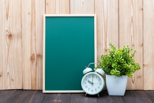 Blank green chalkboard and little tree vintage alarm clock on wood