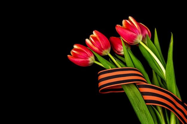 Cartolina d'auguri in bianco al 9 maggio. fiori rossi, nastro di george sul taccuino nero. giorno della vittoria o concetto di giorno del difensore della patria. vista dall'alto, copia spazio per il testo