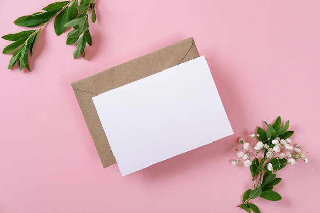 Biglietto di auguri vuoto e busta con gipsofila su sfondo rosa foglio di carta bianco con spazio per la copia del mockup composizione minima del posto di lavoro vista dall'alto piatta