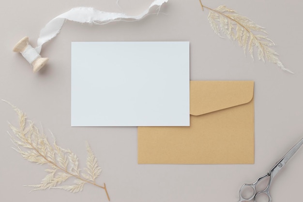 Blank greeting card invitation Mockup 5x7 on Brown envelope with dried flowers on beige background flat lay mockup