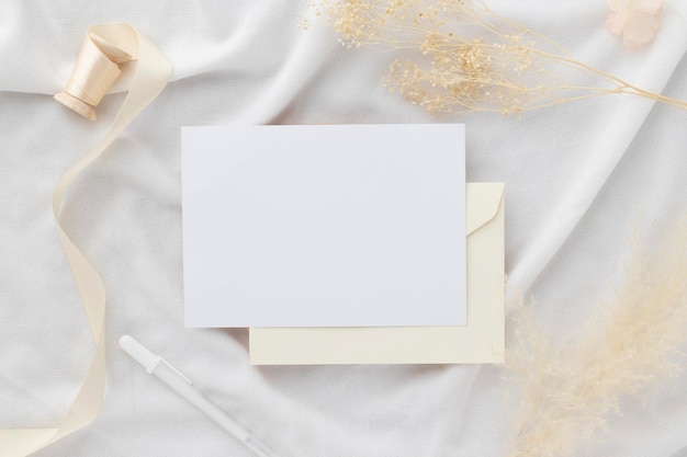 Photo blank greeting card invitation mockup 5x7 on envelope with dry flowers and ribbon on paper background flat lay mockup