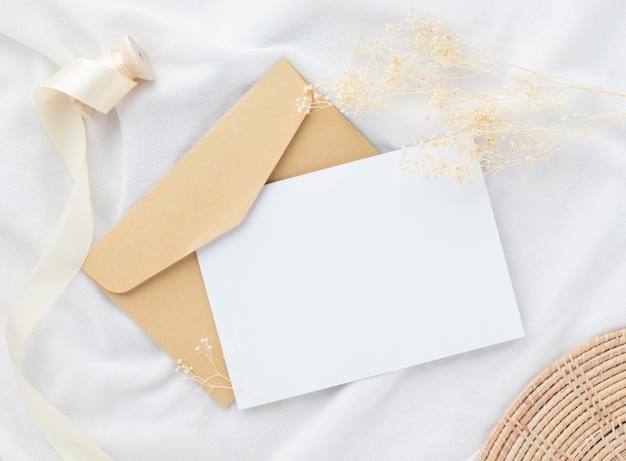 Blank greeting card invitation Mockup 5x7 on envelope with dry flowers and ribbon on white fabric background flat lay mockup