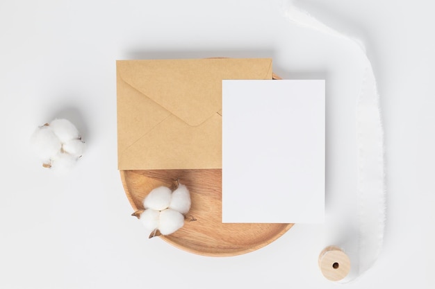 Blank greeting card invitation Mockup on Brown envelope with cotton flower on white background Minimal table workplace composition flat lay mockup