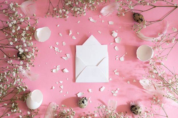 Blank greeting card, kraft envelope. Easter eggs and gypsophila flowers on a pink background. Flat lay, top view.