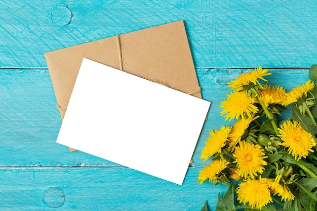 Пустая поздравительная открытка или приглашение на свадьбу с желтыми цветами одуванчика на синем деревянном фоне