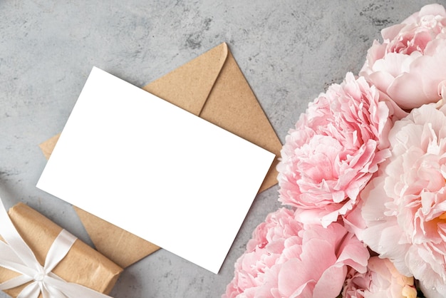 パステルピンクのピオニーの花とグレーの背景のギフトボックスを備えた白いグリーティングカード 結婚式