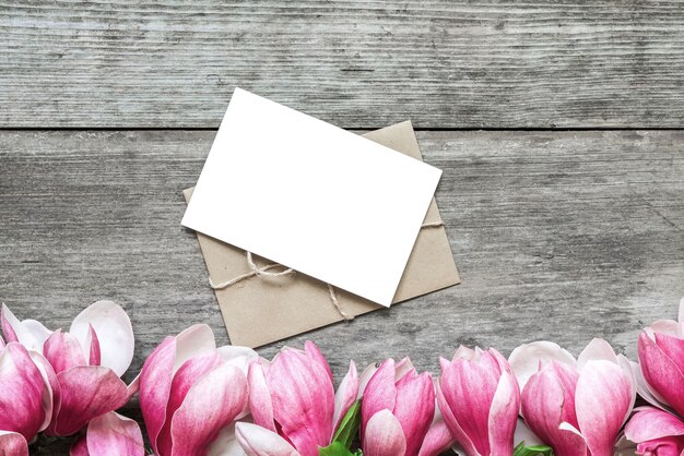 素朴な木製のテーブルにピンクのマグノリアの花を持つ空白のグリーティングカード。平干し。上面図