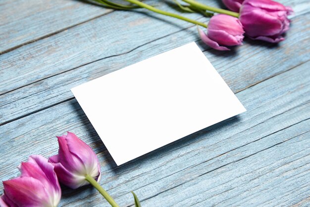 Foto biglietto d'invito vuoto mockup biglietto d'auguri bianco con fiore di tulipano viola su sfondo di legno blu