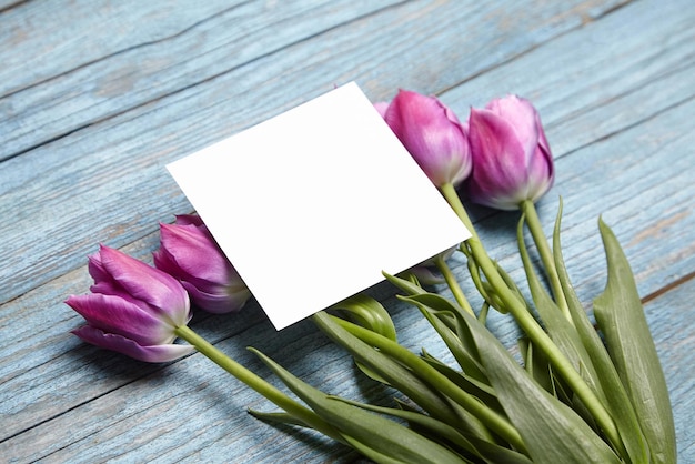 Foto biglietto d'invito vuoto mockup biglietto d'auguri quadrato bianco con fiore viola su sfondo di legno blu