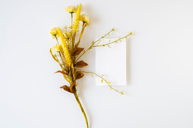 白い背景の上面に黄色い花の花束を持つ空白の招待状のモックアップと