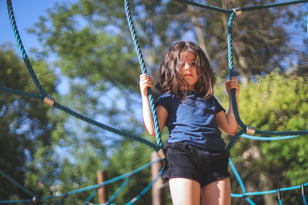 Blank meisje staat op een touwschommel in een park op een speelplaats