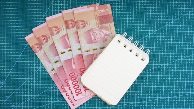 Blank note book with Indonesia money on green grid background