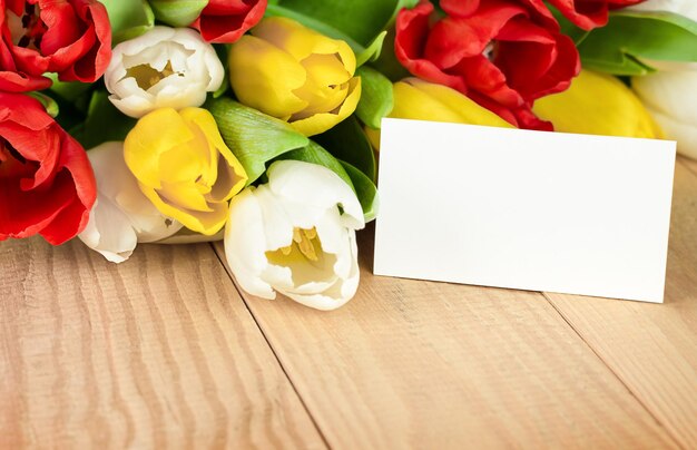 Blank note and bouquet of tulips on wooden table