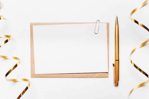 Blank note with envelope, pen, gifts and gold ribbon on white background