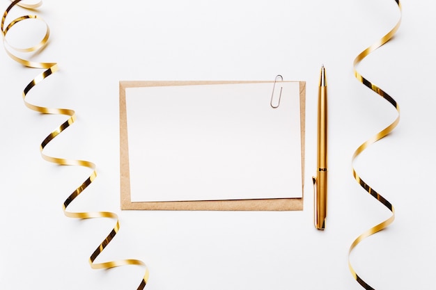 Blank note with envelope, pen, gifts and gold ribbon on white