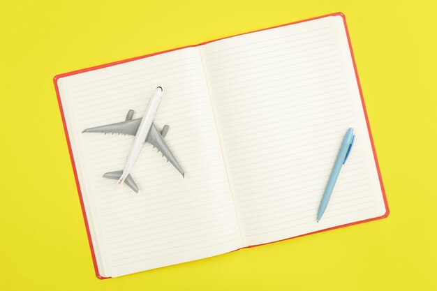 Blank notebook and airplane model on green background flat lay