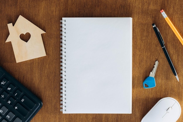 Blank notebook calculator and model of a house on a wooden table flat lay