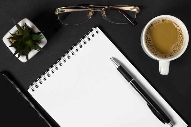 blank notebook and different office supplies on dark background copy space top view