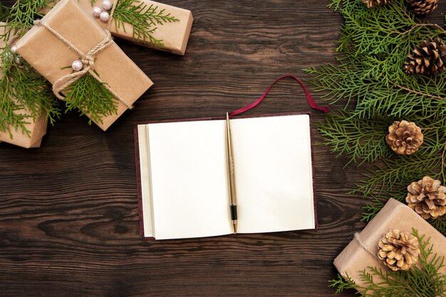 Blank notebook, gifts boxes, branch and fir cones on wooden. top view