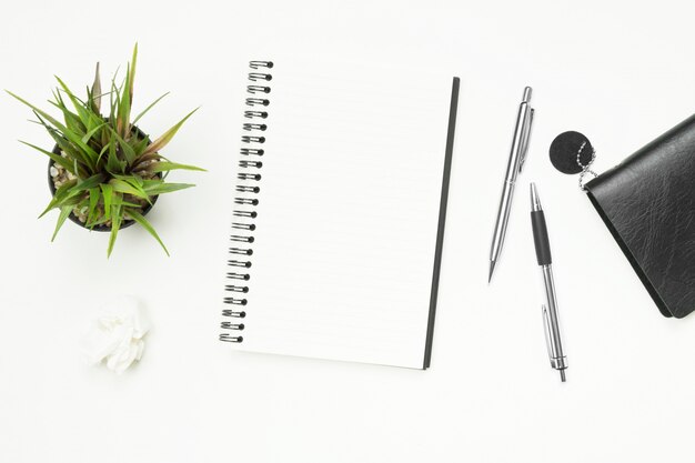 Blank notebook page is on top of white desk table with pen.