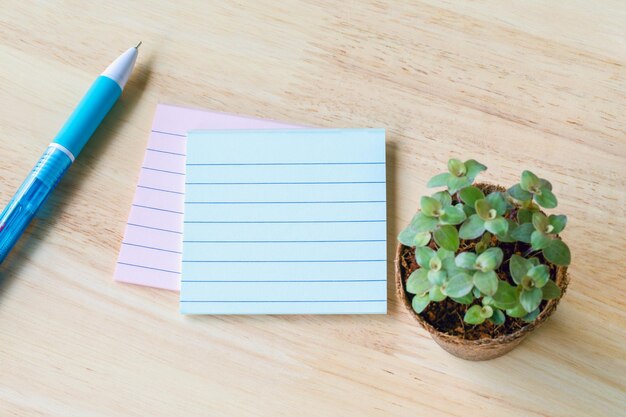 Blank notebook paper with little plants in eco pot on a wooden table picture used for add text or education message green fresh white note with pencil