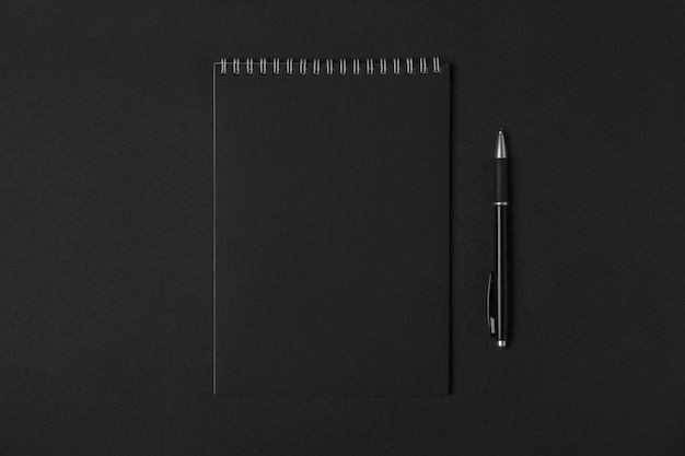 Blank notebook and pen on dark background copy space top view