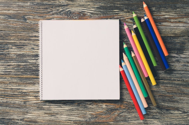 空白のノートブックと木製のテーブルにカラフルな鉛筆のセット。用紙の背景。