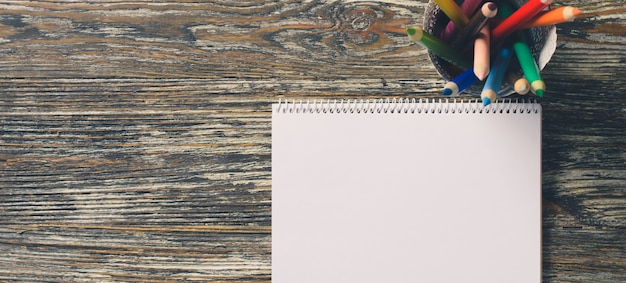 Blank notebook and set of colorful pencils on the wooden table. Paper background.