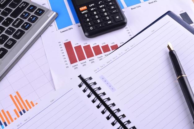 Blank Notebook with calculator, keyboard and fountain pen on graphs, charts and business table. The workplace of business people