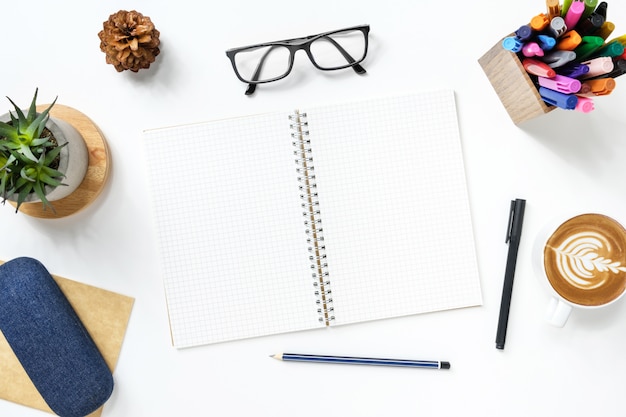 Photo blank notebook with grid lines is on top of white office desk table with supplies.