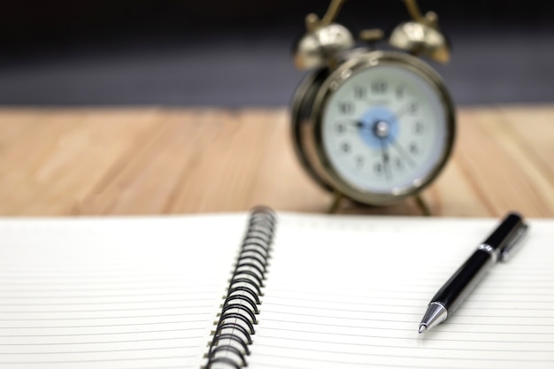 Blank notebook with pen and clock on the table