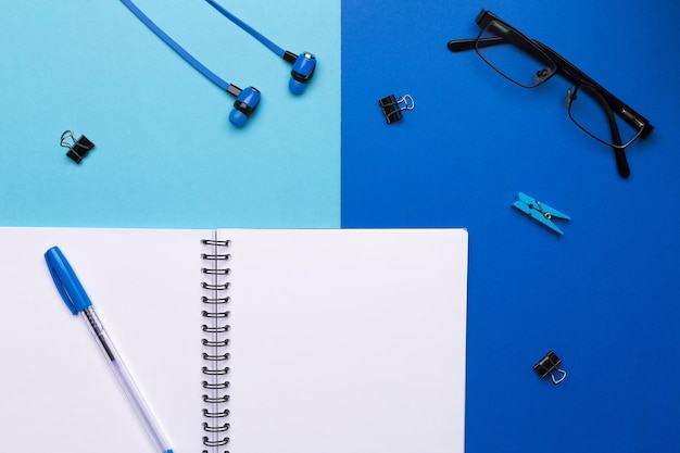 青の背景にペンとヘッドフォンが付いた空白のノート