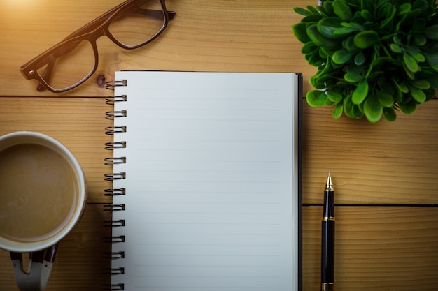 Blank notebook with pen and with glasses next to cup of coffee on wooden table