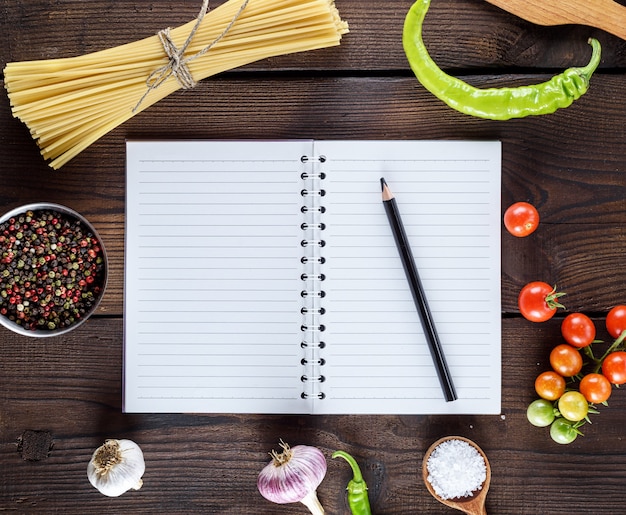 Foto quaderno bianco con lenzuola bianche, pasta lunga cruda e ingredienti per cucinare