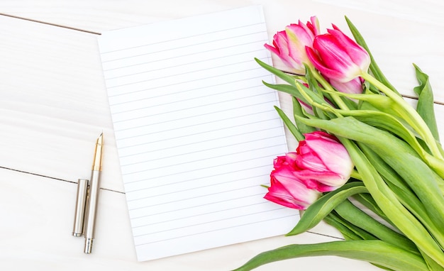 Blank notepad and bouquet with tulips on the wooden table Top view